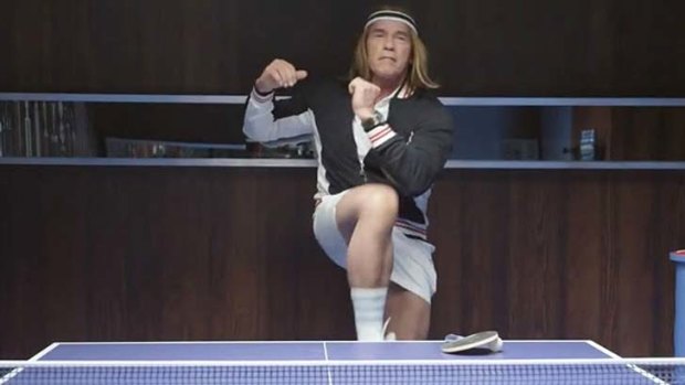Arnold Schwarzenegger wears a long blond wig and poses as a ping pong player.