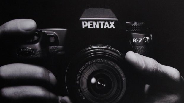 A man walks behind a Pentax camera advertisement.