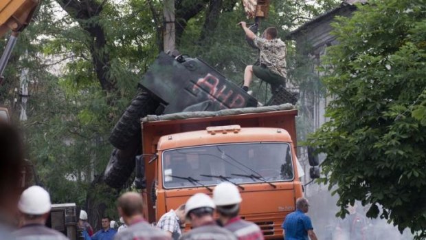 Workers load a burned armoured military vehicle onto a truck in Mariupol.