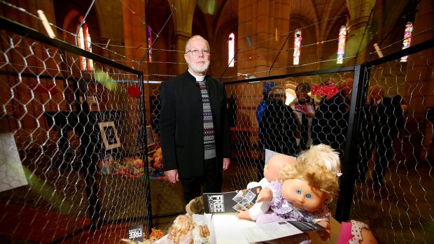 The Very Reverend Dr Peter Catt with a cage filled with 895 dolls, representing children in asylum. 