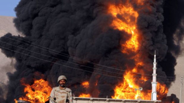 Firing up ... a Pakistani paramilitary soldier stands guard in front of a burning NATO supplies oil tanker following  a gunmen attack in Quetta.