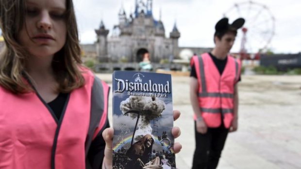 A performer holds a brochure for 'Dismaland', a theme park-styled art  installation by British artist Banksy.