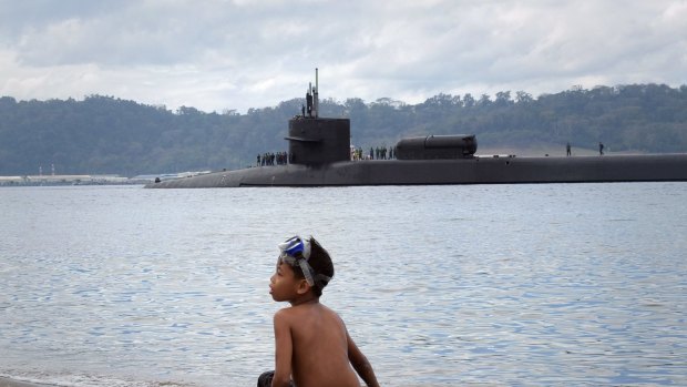 A child sits on the beach as the USS Ohio passes by in Subic Bay, Philippines.