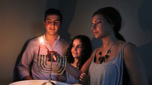 Embracing tradition &#8230; Simon, 18, Hannah, 12, and Bec Dukes, 20, light a candle to celebrate the first night of Hanukkah.