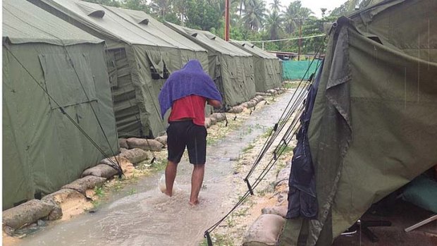 An asylum seeker walks through water running between rows of tents.