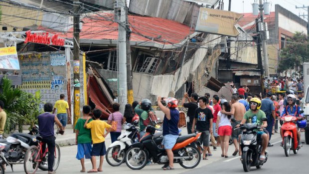 People gather next to damaged buildings in Cebu City.