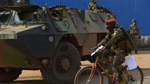 A Seleka soldier rides a bicycle past French troops patrolling in Bangui. 