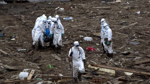 Grim Task ... Japanese police, wearing protective clothing, carry a body recovered from the rubble in a rise paddy in the Fukushima Prefecture.