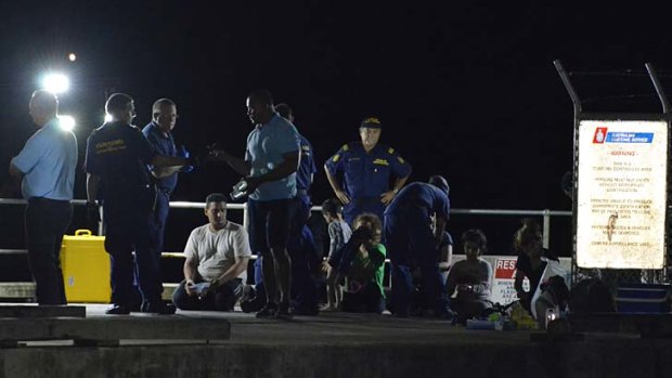 Customs officials and rescue personnel watch over survivors of the capsized boat at Christmas Island docks