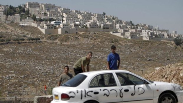 Young Palestinians stand next to one of 10 cars in occupied East Jerusalem sprayed with racist slogans. The Hebrew reads: "All the Arabs are enemies."