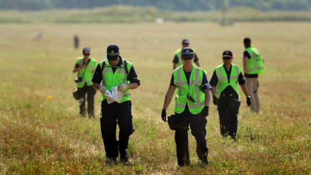 An Australian Federal Police officer reads a Harvey World Travel document as he walks through the fields where MH17 crashed.
