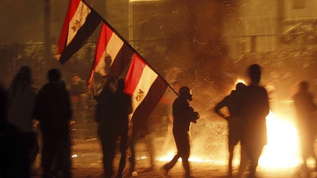 Fog of tear-gas &#8230; a protester carries national flags past flames from a petrol bomb near Tahrir Square in Cairo.
