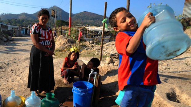 People wait to fill up bottles of water at a settlement in San Salvador.