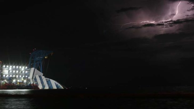 A lightning storm is pictured over the sea near the capsized cruise liner Costa Concordia lying surrounded by cranes outside Giglio harbour.