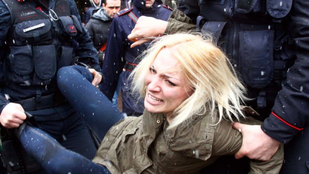 Police take away a woman protesting where former Italian Premier Silvio Berlusconi was voting, in Milan, Italy.