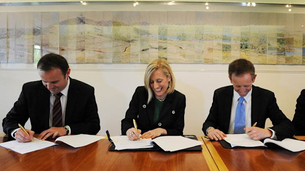 Gallagher signs the agreement with Rattenbury, right, and Deputy Chief Minister Andrew Barr, left.