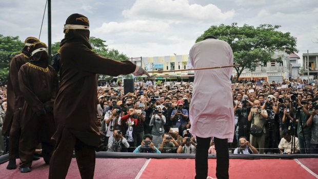 A Shariah law official whips one of two men convicted of gay sex during a public caning outside a mosque in Banda Aceh, Aceh.