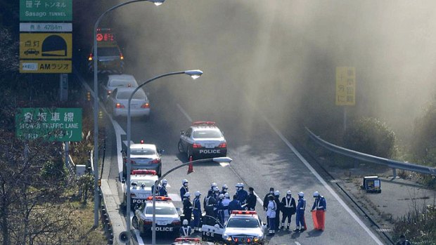 Police vehicles are parked at the entrance as smoke billows out of the Sasago Tunnel on the Chuo Expressway. Several people were feared trapped inside after part of the tunnel collapsed.