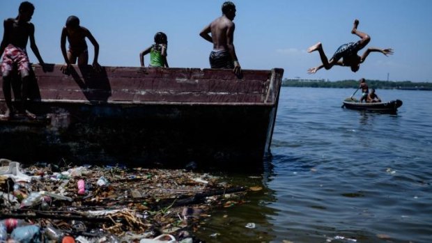 A boy jumps from a boat into polluted water of Guanabara bay in Rio de Janeiro