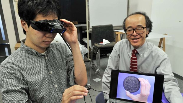 Tokyo University professor Michitaka Hirose (R) and his team developed a camera-equipped special goggle, which makes cookies bigger to help users' diet.