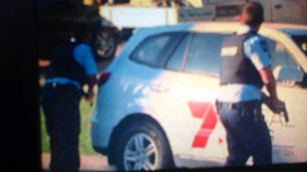 Police take cover behind a Seven News vehicle during a stand-off near Rockhampton.