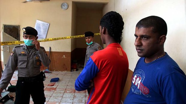 Buddhists killed: Sri Lankan immigrants, right, look on as Indonesian police investigate the crime scene at a detention centre in North Sumatra.