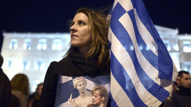 A woman holds a Greek flag and a placard depicting the German chancellor Angela Merkel during a demonstration in front of the Greek parliament prior to the Eurogroup agreement.