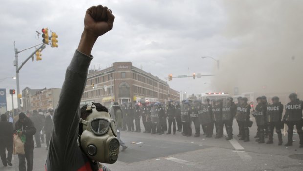 A demonstrator raises his fist as police stand in formation as a store burns, during unrest following the funeral of Freddie Gray in Baltimore.
