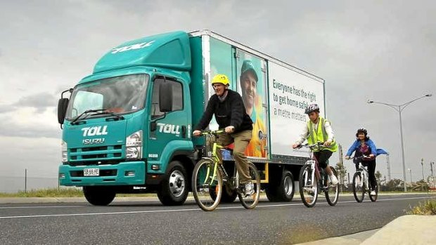 Cycling family Mark, daughter Gabi and wife Anna Watson near a Toll truck with the signage.