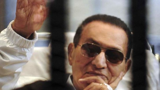 Former Egyptian President Hosni Mubarak waves to his supporters inside a cage in a courtroom at the police academy in Cairo, in April.