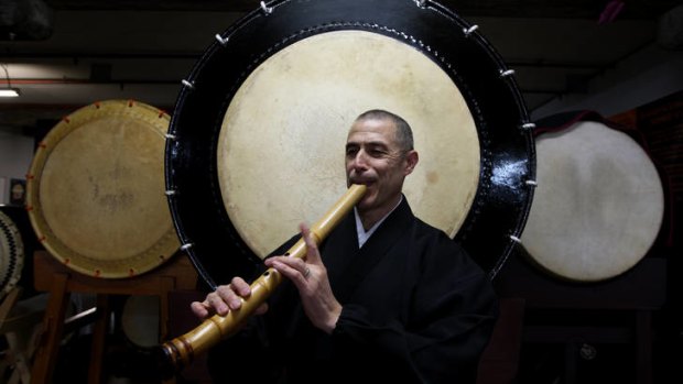Dr Riley Lee plays the shakuhachi in front of taiko drums.