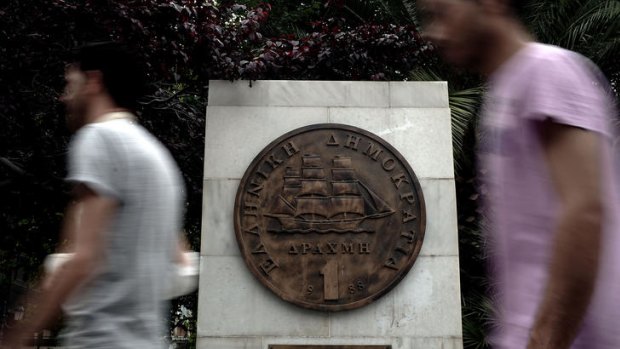 People walk past a monument featuring a replica of the last edition of the Greek currency, the drachma, in the centre of Athens.