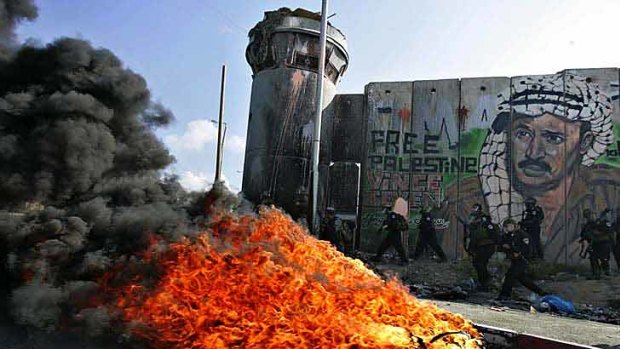 Under a mural of late Palestinian leader Yasser Arafat, Israeli soldiers pass burning tyres left by protesters at a checkpoint between Ramallah and Jerusalem.