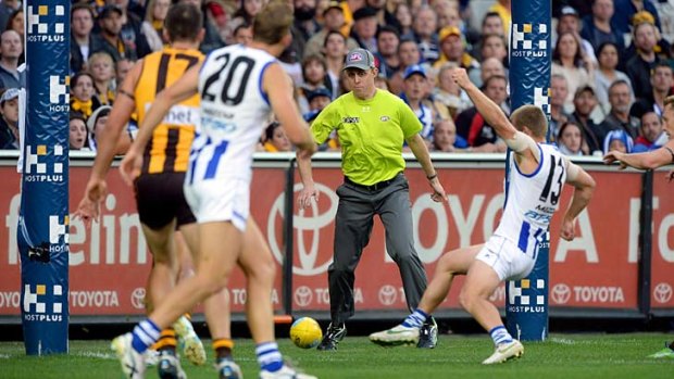 Goal umpire Michael Palm watches the ball carefully as North Melbourne's Leigh Adams gets his foot to it.