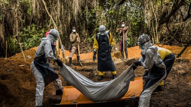 A burial team transfer Mama Flomo, a 37-year-old mother of three who died before she reached  help, to her grave adjacent to the Bong County Ebola Treatment Unit in Suakoko, Liberia.
