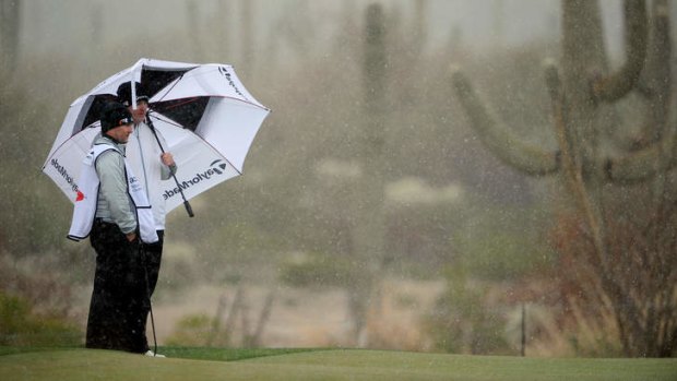 Marcus Fraser of Australia shelters from the snow with his caddie.