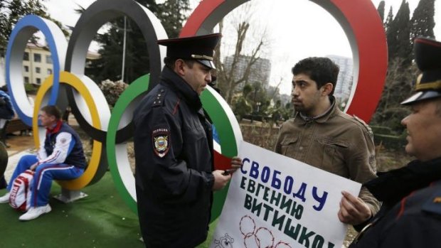 Activist David Khakim, right, is approached by two police officers after pulling out a banner protesting against a recent prison sentence for a local environmentalist in front of the Olympic rings in central Sochi.
