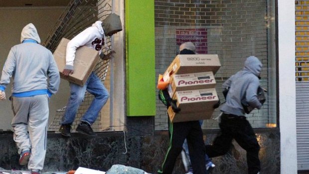 Looters carry boxes out of a home cinema shop.