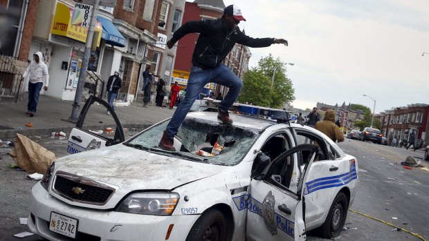 Rioter jumps on a damaged police department vehicle during clashes in Baltimore.