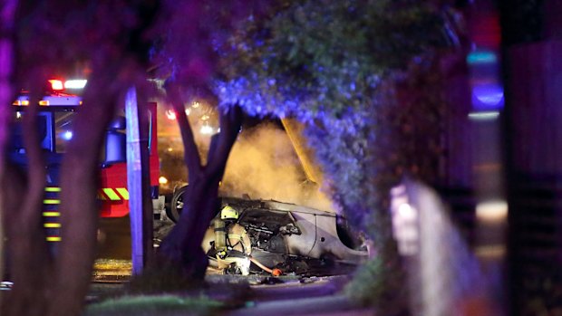 Firefighter looks inside car whilst it smolders.