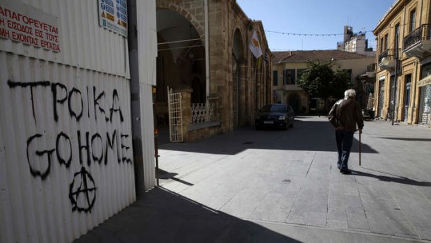 A man walk past a graffiti which reads "Troika go home" in the Cypriot capital of Nicosia on March 16, 2013. Eurozone finance ministers agreed on a bailout for Cyprus, the fifth international rescue package in three years of the debt crisis. AFP PHOTO/YIANNIS KOUTOGLOU