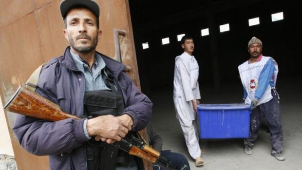Contentious: Afghan election commission workers carry a ballot box as a police officer stands guard.