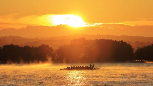 A pair of dragon boats race neck and neck across Lake Burley Griffin, under a scorching summer sunrise.