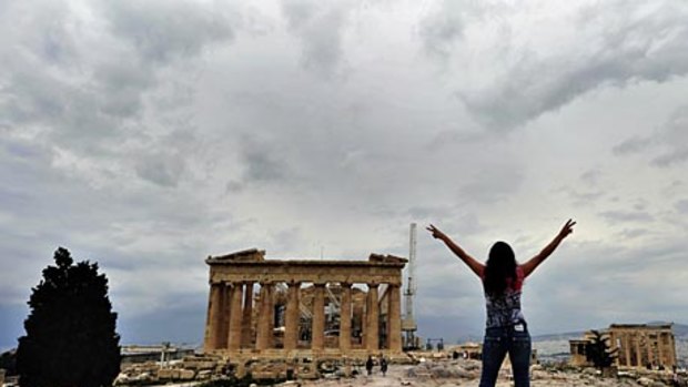 A tourist poses for a photo atop the Acropolis hill with the ancient Parthenon temple in the background,