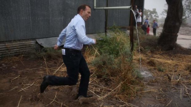 Prime Minister Tony Abbott dashes through a downpour after meeting graziers and community members at a property near Bourke NSW.