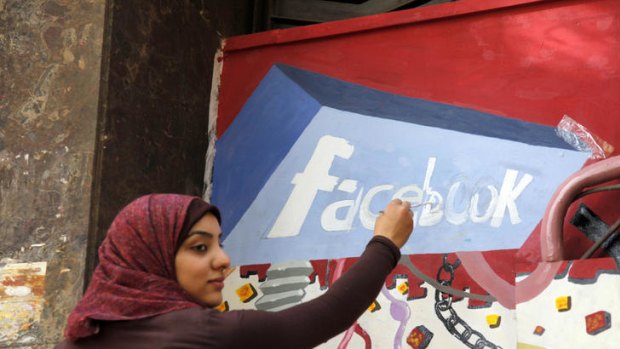 An Egyptian student paints the Facebook logo on a mural commemorating the revolution that overthrew Hosni Mubarak. Social media played an important role in co-ordinating action.