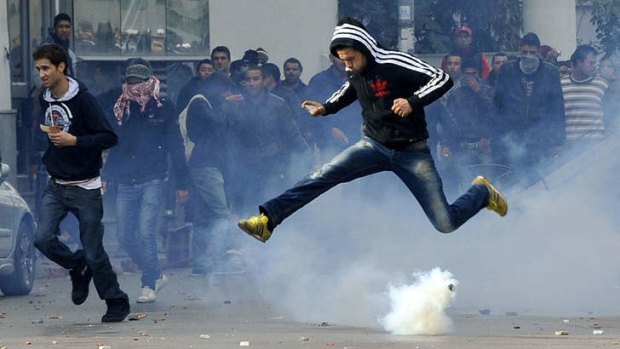 A Tunisian protester jumps through tear gas.