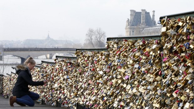 A tourist attaches a love lock on a fence on the access ramp to the Pont des Arts over the River Seine in Paris which is covered with thousands of padlocks.