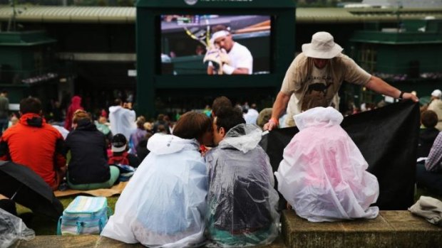 Fans sit in the rain on Murray mound watching the Rafael Nadal of Spain against Mikhail Kukushkin of Kazakhstan match on the big screen as rain delays the start of play on day six of the Wimbledon Lawn Tennis Championships. 