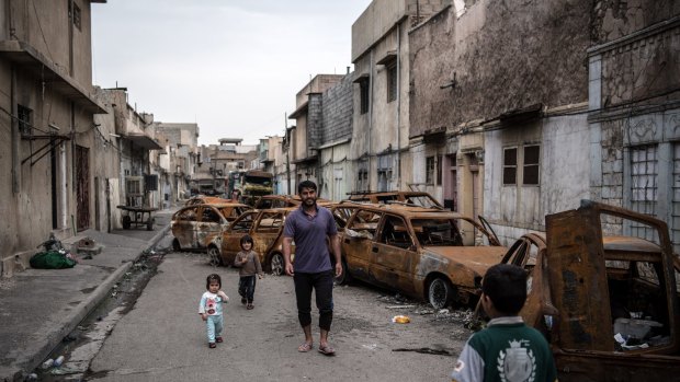 A man walks with his children past burnt-out cars in a street in west Mosul earlier this month.